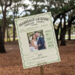 Pinellas County Marriage License. A photo of a marriage license issued by Pinellas County, Florida. The document is printed on beige paper and has a green border. There's a photo of the bride and groom, who are smiling. The bride is wearing a white dress and the groom is wearing a suit. The background is a wooded area with trees.